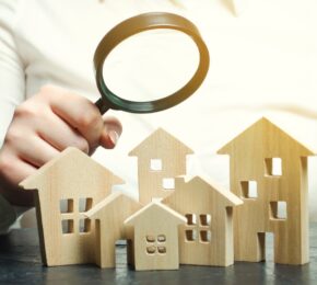 A Woman Is Holding A Magnifying Glass Over A Wooden Houses. Real