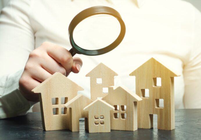 A Woman Is Holding A Magnifying Glass Over A Wooden Houses. Real