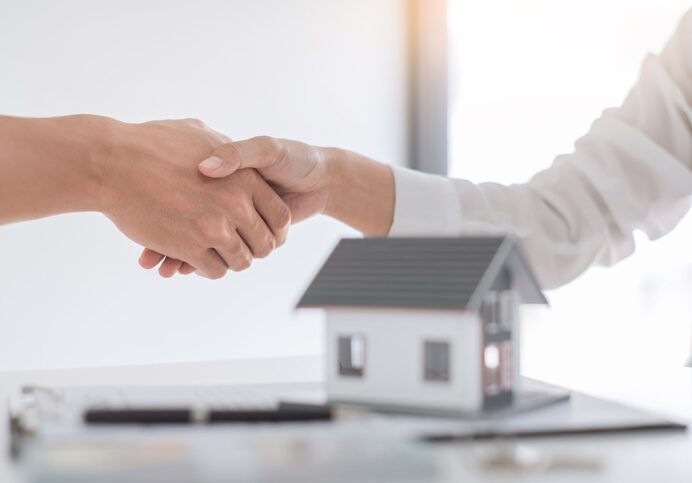 Estate agent in suit sitting in an office desk shaking hands with customer after contract signature accept agreement finish buying or rental real estate for transfer right of property